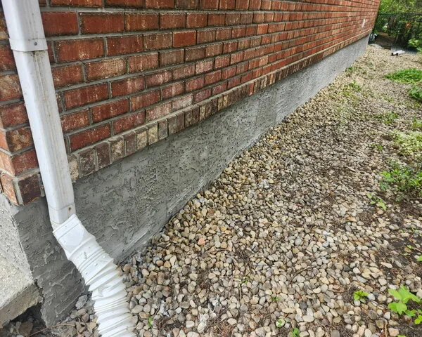 New textured parging to house foundation, white downpipe seen right of photo, and red brick siding above parged foundation