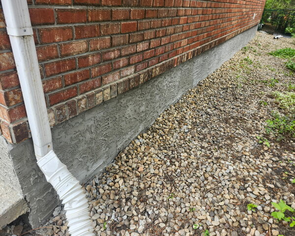 New texted parging to house foundation, white downpipe seen right of photo, and red brick siding above parged foundation